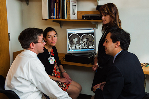 Four staff members confer in front of a screen showing scans of a patient's cranium. Four staff members confer in front of a screen showing scans of a patient's cranium.